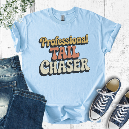 Light blue t-shirt with 'Professional Tail Chaser' text, paired with jeans and sneakers on a wooden surface.