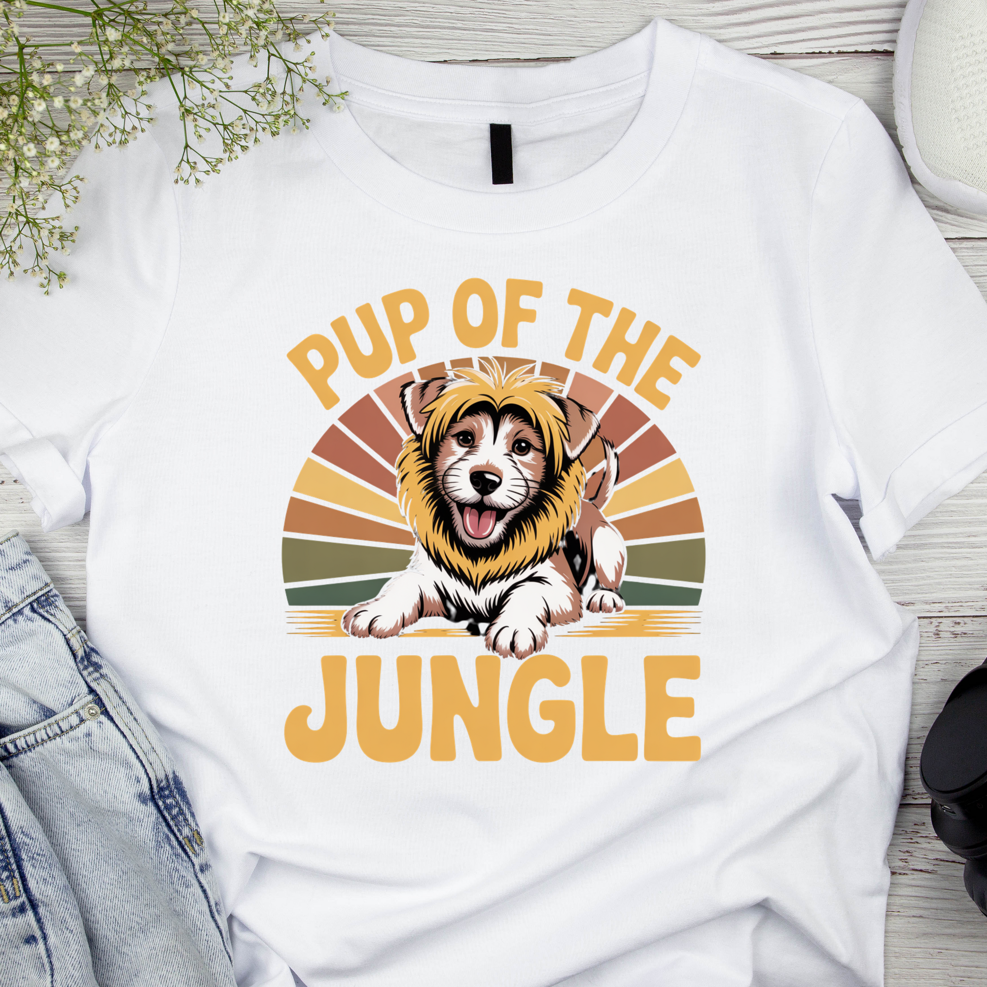 White t-shirt with a graphic of a dog wearing a lion mane and text 'Pup of the Jungle' on a wooden surface.
