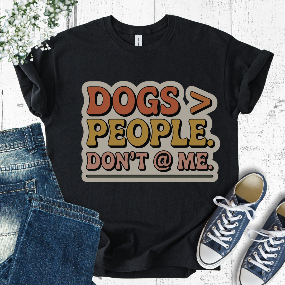 Black t-shirt with 'DOGS > PEOPLE. DON'T @ ME.' text, paired with jeans and sneakers on a light wooden surface.
