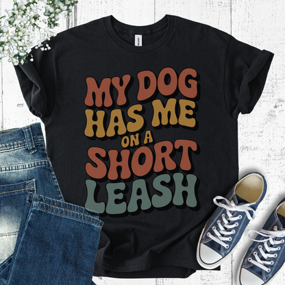 Black t-shirt with colorful text 'My dog has me on a short leash' displayed with jeans and sneakers.