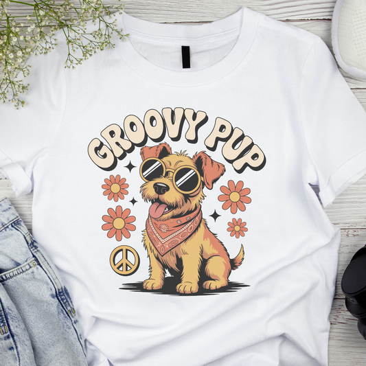 White t-shirt with a cartoon dog wearing sunglasses and a bandana, surrounded by flowers and peace symbols, on a wooden surface.