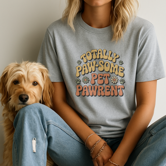 Person wearing a gray t-shirt with 'TOTALLY PAW-SOME PET PAWRENT' text sitting next to a dog.