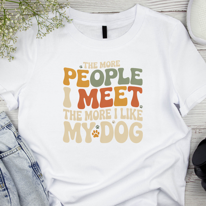 White t-shirt with colorful text design on a wooden surface with denim jeans and flowers.