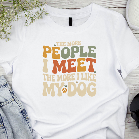 White t-shirt with colorful text design on a wooden surface with denim jeans and flowers.