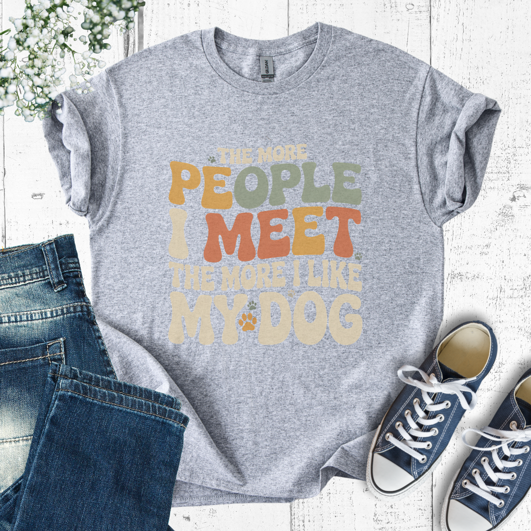 Gray t-shirt with colorful text design on a white wooden surface with jeans and sneakers.