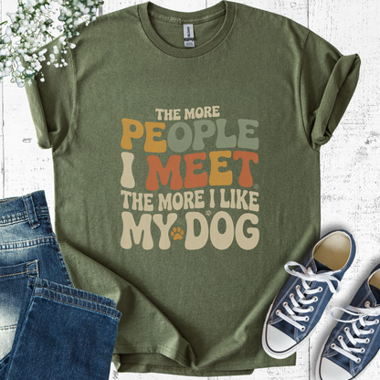 Green t-shirt with humorous text, jeans, and sneakers on a light wooden surface.