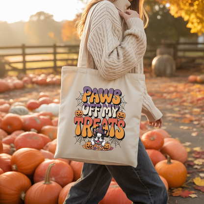 Person holding a tote bag with 'Paws off my treats' design in a pumpkin patch.