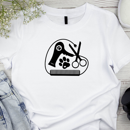 White t-shirt with a black paw print and grooming tools design on a wooden surface.