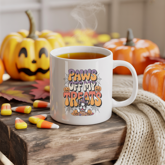 White mug with Halloween-themed design featuring pumpkins and text, placed on a wooden surface with pumpkins and candy corn in the background.