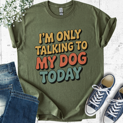 Green t-shirt with 'I'm only talking to my dog today' text, paired with jeans and sneakers on a light wooden surface.