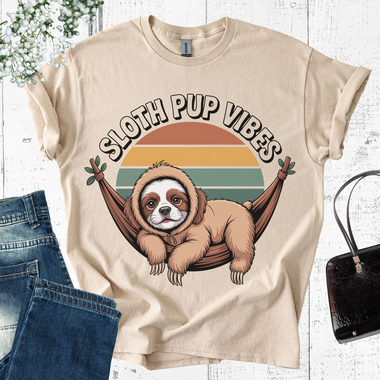 Beige t-shirt with sloth and dog hybrid graphic and 'Sloth Pup Vibes' text on a white wooden background.