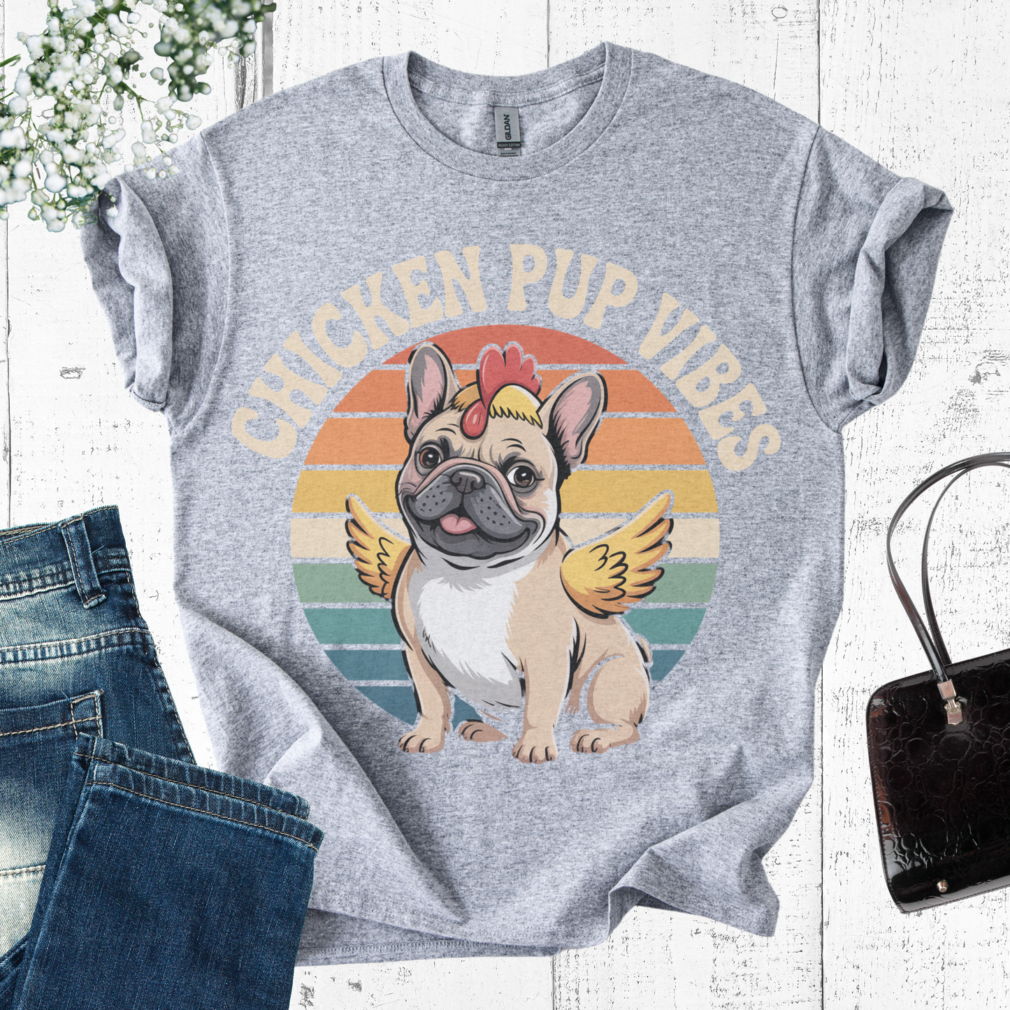 Gray t-shirt with a cartoon dog and chicken design, text 'Chicken Pup Vibes', on a white wooden surface with jeans and a handbag.