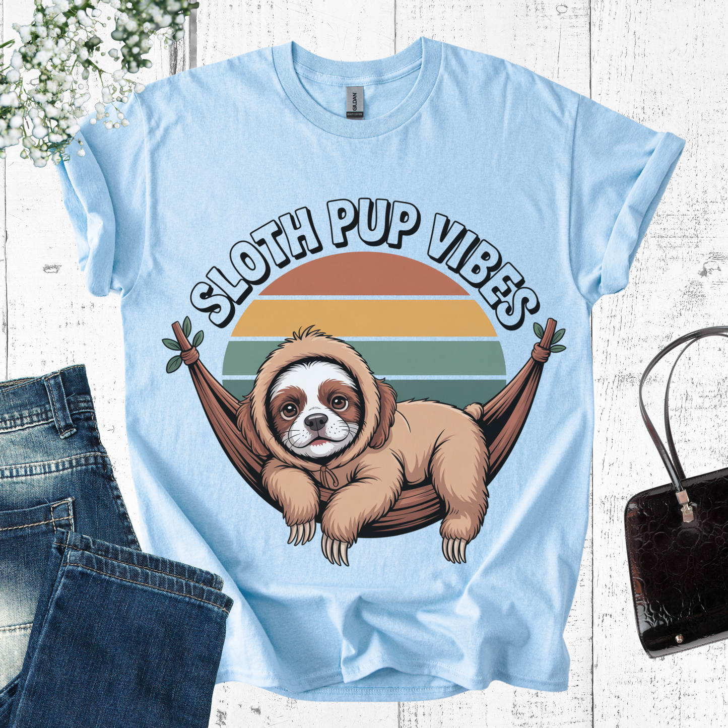 Light blue t-shirt with a sloth in a hammock graphic and 'Sloth Pup Vibes' text on a wooden surface.