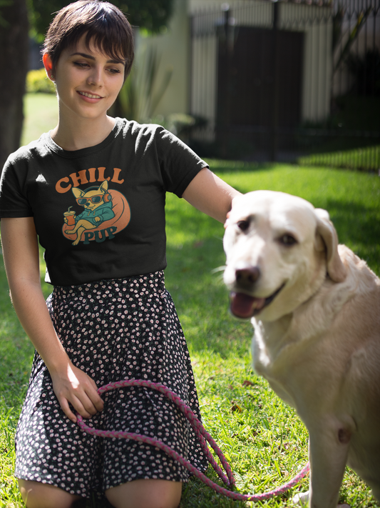 Woman in a black t-shirt with a dog on a leash in a grassy area wearing a tee with the phrase 'Chill Pup'.