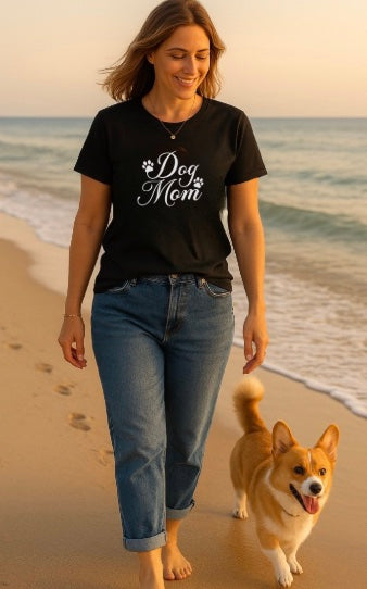 Woman walking on the beach with a dog, wearing a black t-shirt with 'Dog Mom' text.