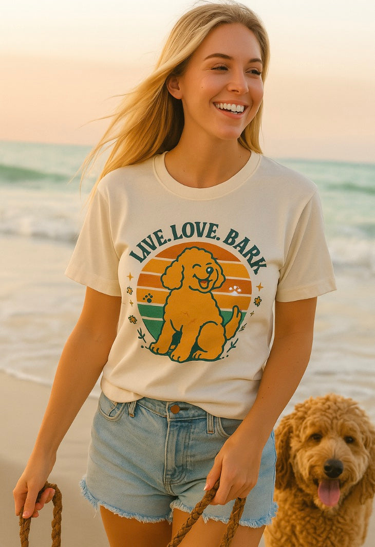Woman wearing a 'Live. Love. Bark' t-shirt with a dog graphic on a beach.