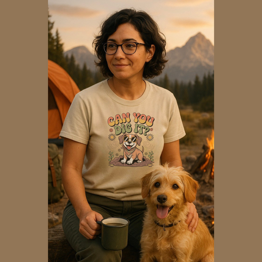 Person wearing a t-shirt with a dog graphic and text, sitting with a dog by a campfire with mountains in the background.