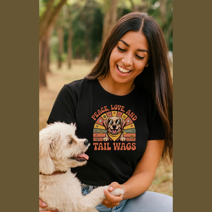 Woman wearing a black t-shirt with a dog graphic and text, sitting outdoors with a small white dog. The phrase says "Peace, Love and Tail Wags".